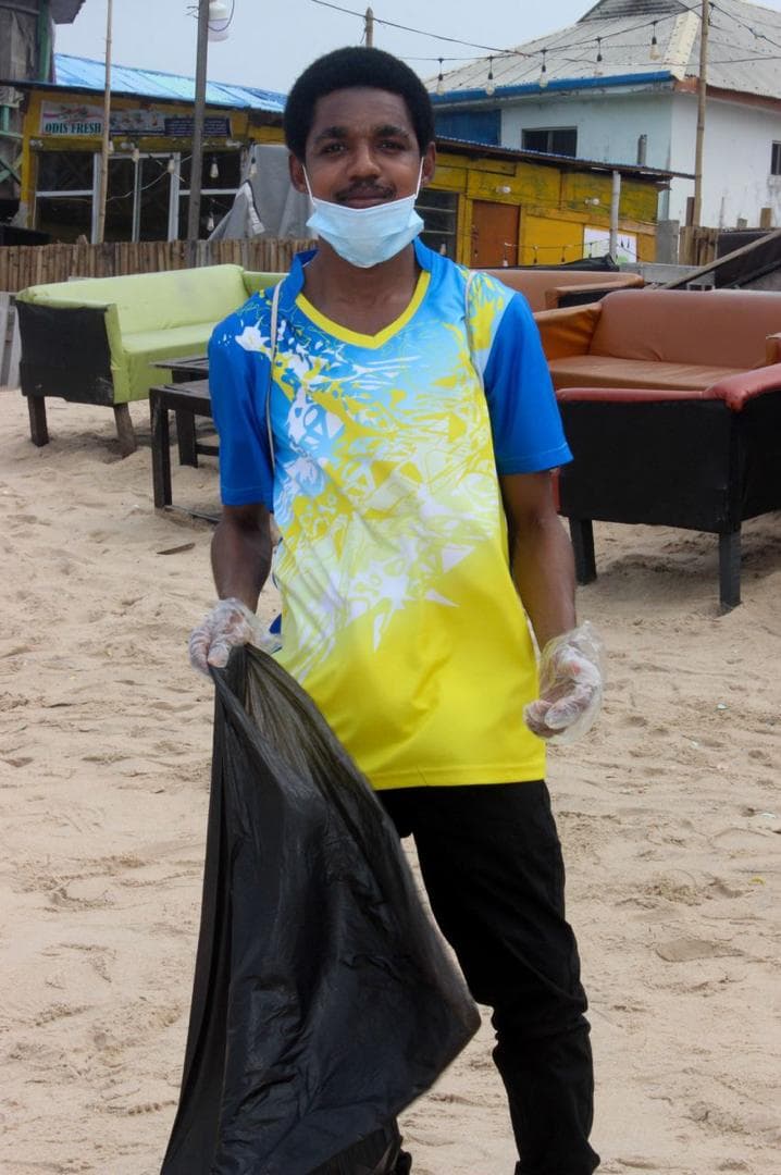 A young volunteer in gloves and a face mask holding a rubbish bag on a beach