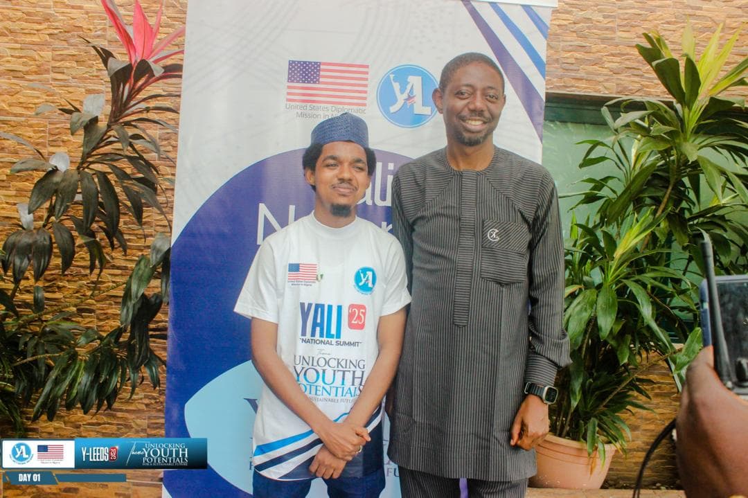 Maharaz in a YALI T-shirt standing with a man in front of a YALI banner